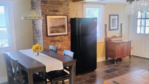 A kitchen with a brick wall, a black refrigerator, and a dining table with chairs.