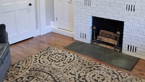 A living room with a white brick fireplace, a mounted flat-screen TV, and a patterned rug.