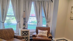 A living room with two patterned armchairs, a rug, and a window with curtains.