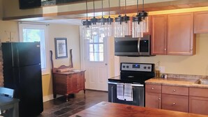 A kitchen with a wooden table, chairs, a refrigerator, a microwave, and a hanging light fixture.