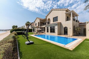 Ein modernes, zweistöckiges Haus mit Swimmingpool, einem gepflegten Rasen und Blick auf den Strand.