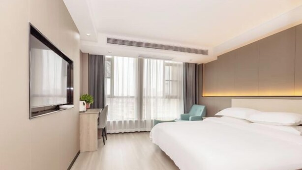 A hotel room with a bed, a desk with a chair, a TV, and a window with curtains. - Carnival Hotel (Chizhou)
