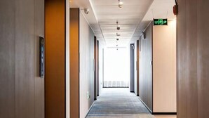 A hotel corridor with a carpeted floor, wooden walls, and a ceiling with recessed lighting. - Carnival Hotel (Chizhou)