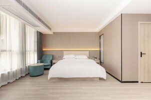 Una habitación de hotel moderna con una cama grande, una mesita auxiliar redonda y una zona de estar con una silla.