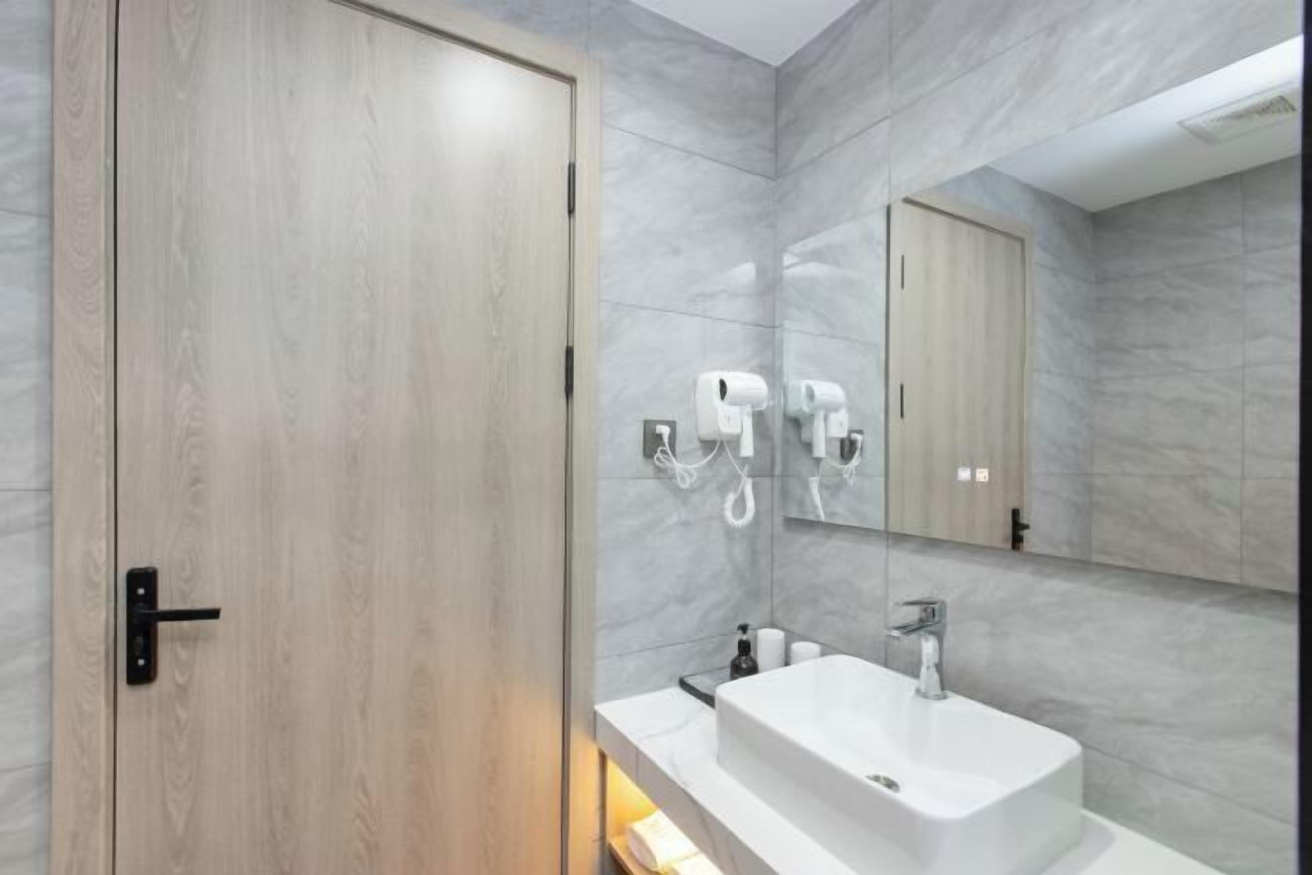 A modern bathroom with a wooden door, a white sink, and a mirror.