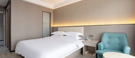 A modern hotel room with a large bed, a bedside table with a lamp, and a teal armchair.