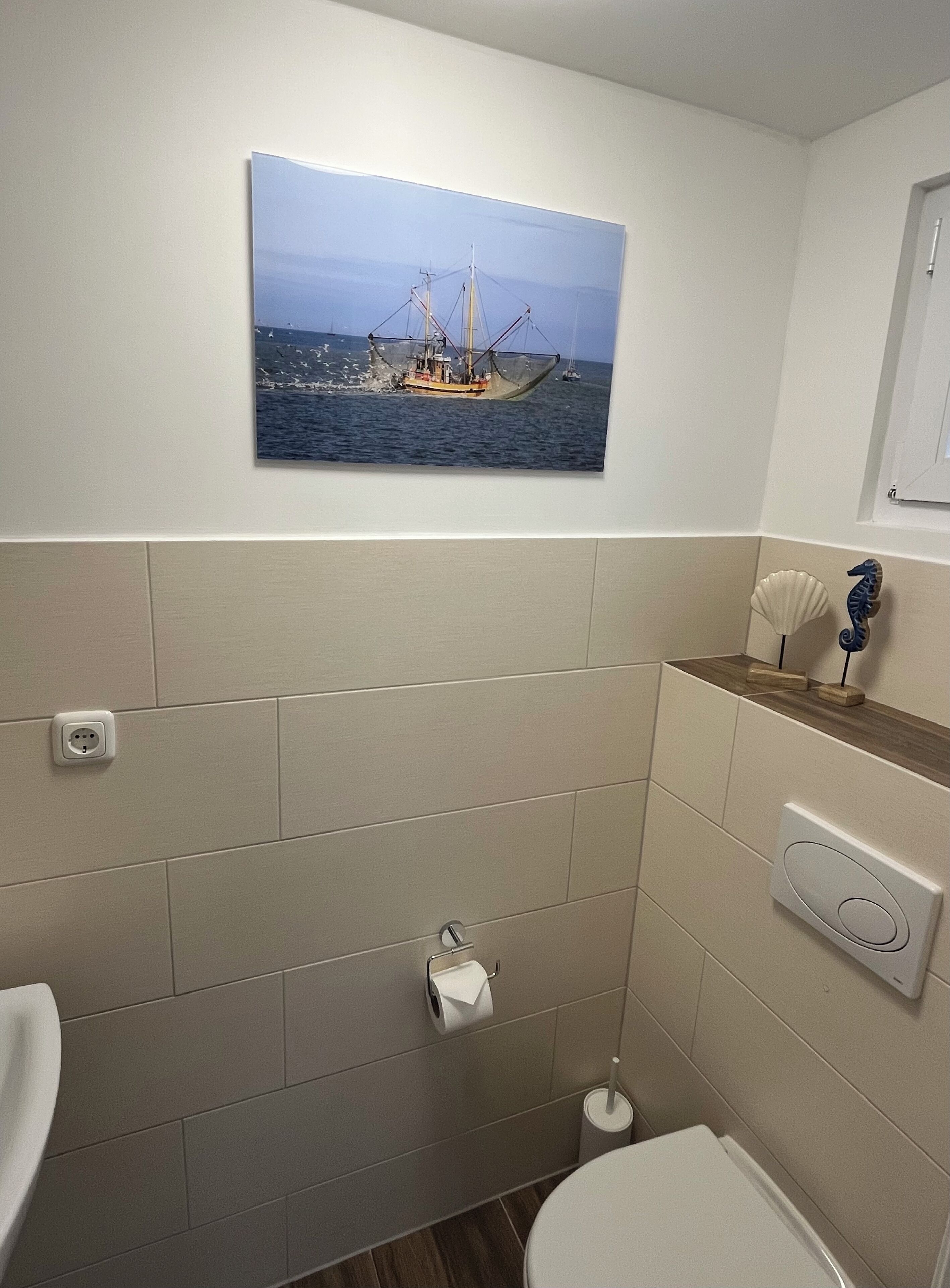 A bathroom with a nautical-themed wall art, a toilet, a bidet, and a small shelf with decorative items.