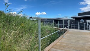 A wooden boardwalk leading to a modern building with metal railings and a clear blue sky.