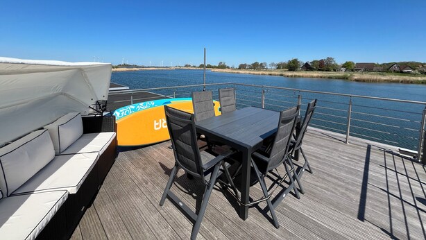 A deck with a table and chairs, overlooking a body of water with houses in the background.