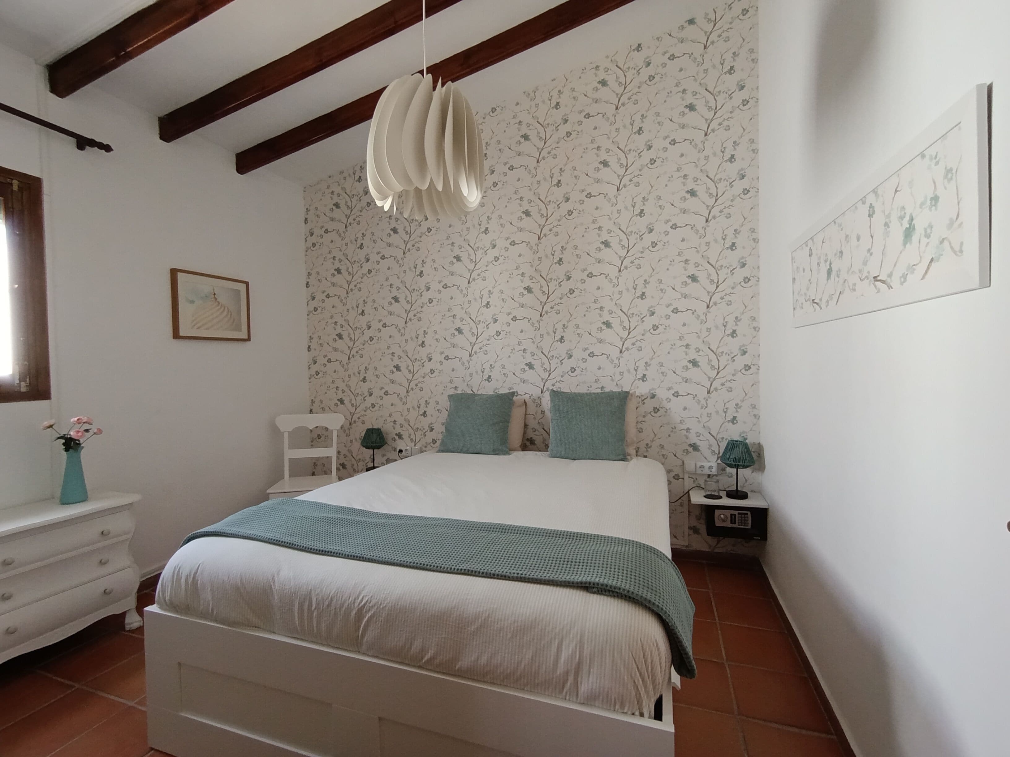 Een slaapkamer met een bed, een kaptafel, een nachtkastje, een lamp en een bloemen behang wand.
