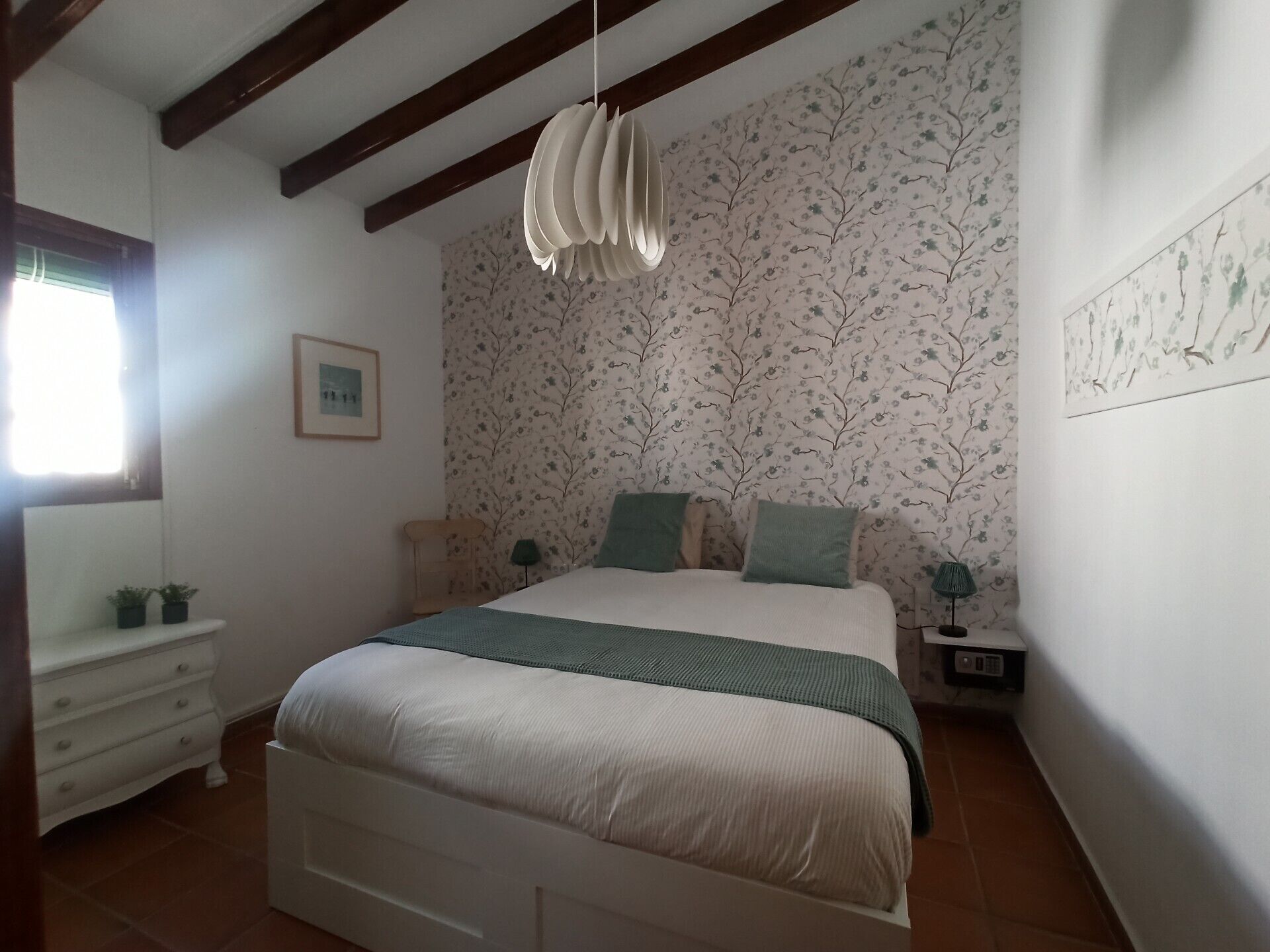 A bedroom with a bed, a nightstand, a dresser, and a hanging light fixture.