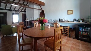 Un coin repas avec une table et des chaises en bois, un vase de fleurs, un meuble à bouteilles et un réfrigérateur rempli de boissons.