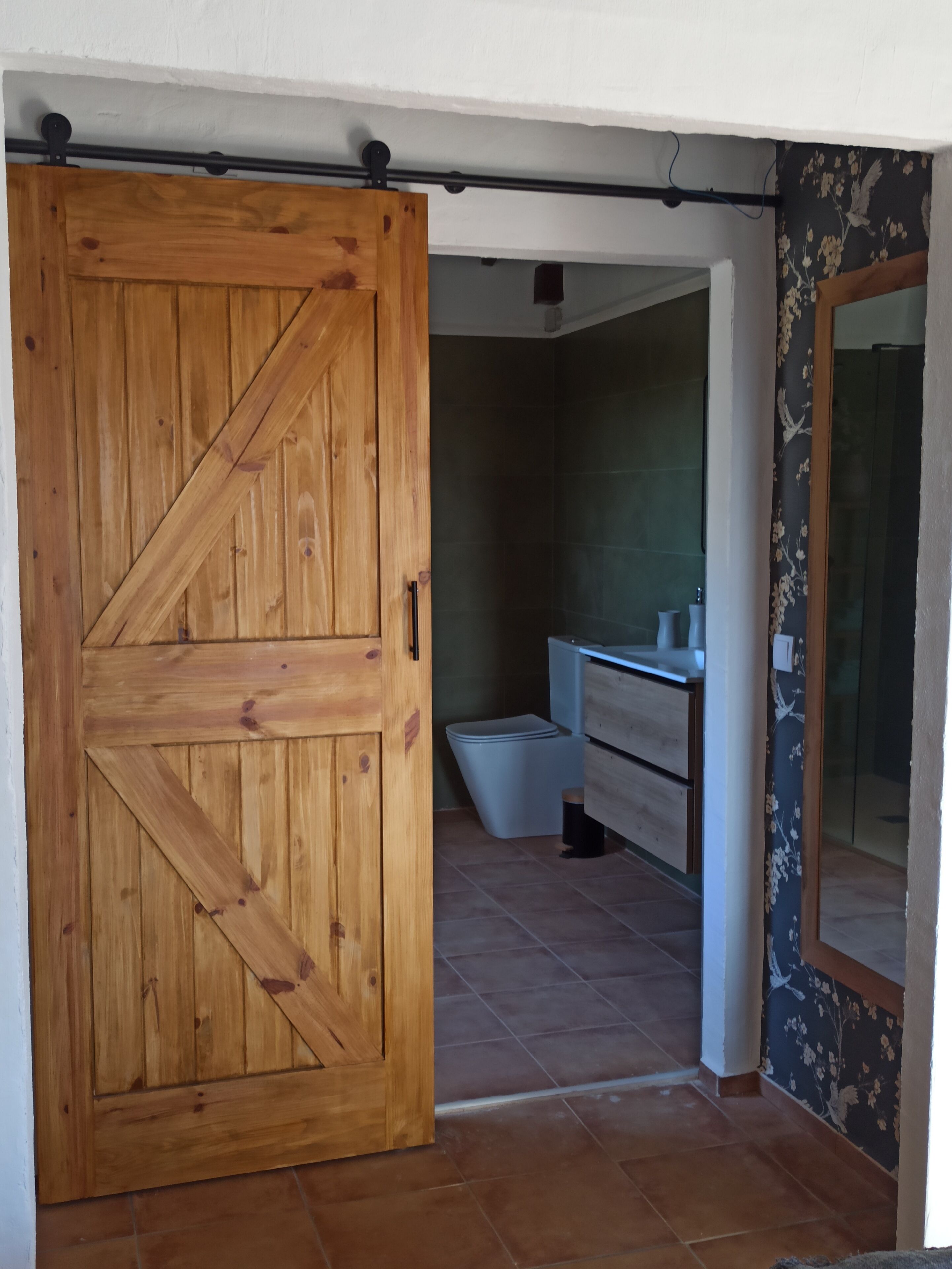 Porta de madeira que dá para um banheiro com vaso sanitário, pia e chuveiro.