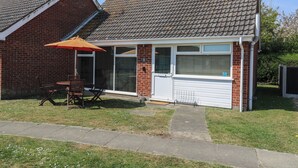 Une maison de plain-pied avec une façade en briques, un toit en tuiles et un petit patio comprenant une table et des chaises.