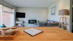 Un salon moderne avec une table à manger en bois, un canapé gris et un téléviseur fixé au mur.