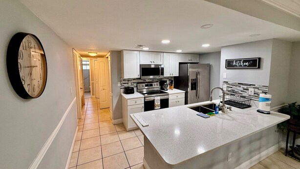 A modern kitchen with white cabinets, stainless steel appliances, and a large island with a sink.