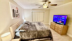 A bedroom with a bed, a ceiling fan, a TV, and a dresser.