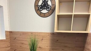 Une table à manger en bois, accompagnée de deux chaises, un vase vert contenant de l’herbe et une horloge murale.