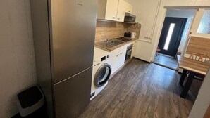 Une cuisine de taille réduite, dotée d’un réfrigérateur en acier inoxydable, d’un lave-linge et de meubles de rangement en bois.