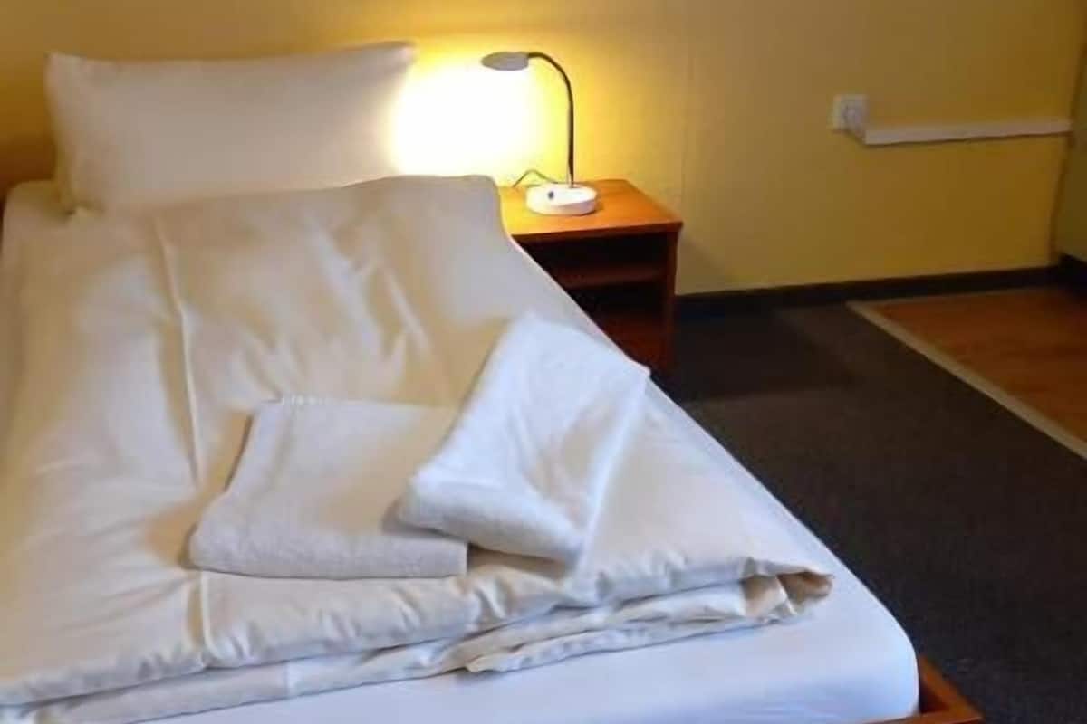 A neatly made bed with white linens, a wooden headboard, and a bedside table with a lamp.
