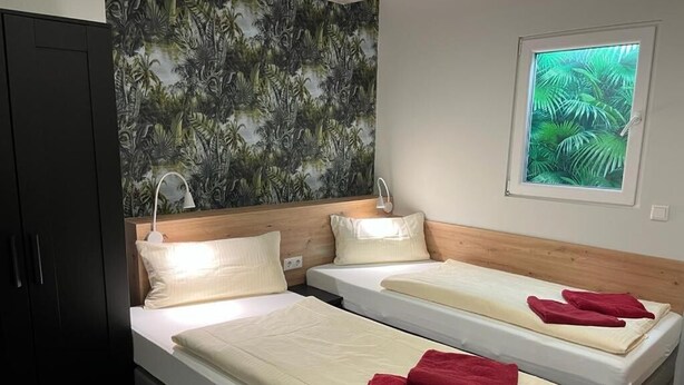 Une chambre d’hôtel avec deux lits simples, une tête de lit en bois, une grande fenêtre donnant sur un paysage verdoyant et une armoire sombre.