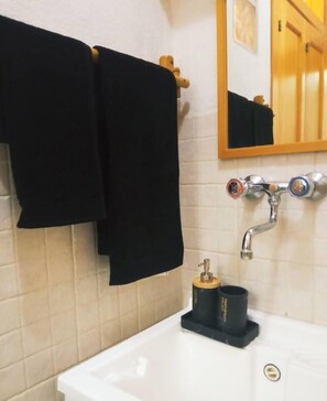 Een badkamer met een witte wastafel, een spiegel erboven en een handdoekrek met een zwarte handdoek.