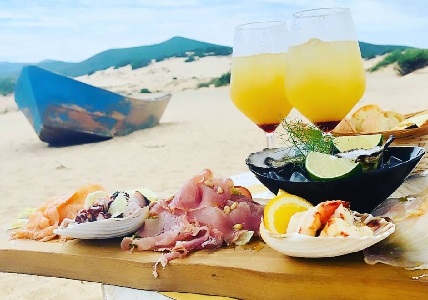 A beachside meal setup with seafood, a drink, and a boat in the background.