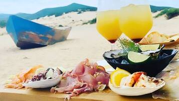 A beachside meal setup with seafood, a drink, and a boat in the background.