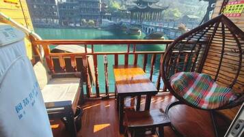 A balcony with a wooden railing, a hanging chair, and a table with a cushion.