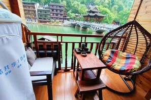 Uma varanda com mesa de madeira, cadeira acolchoada e vista para edifícios tradicionais e uma ponte sobre a água.