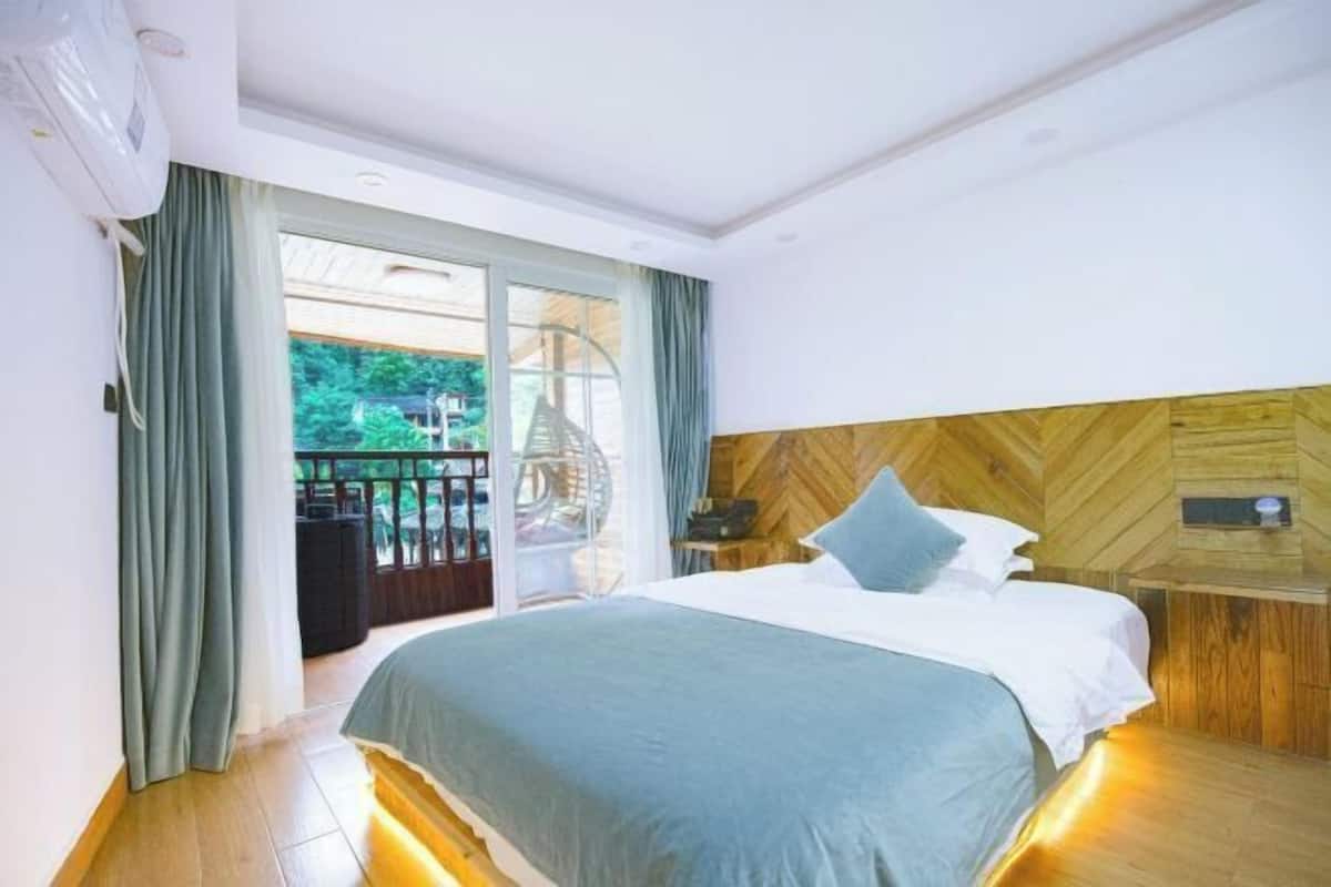 A bedroom with a bed, a wooden headboard, a nightstand, and a view of the outdoors.