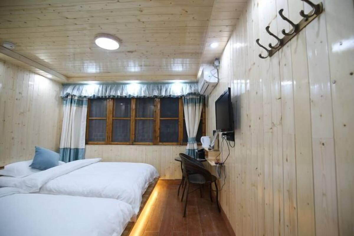 A room with wooden walls, a bed, a desk, a chair, a TV, and a window with curtains.