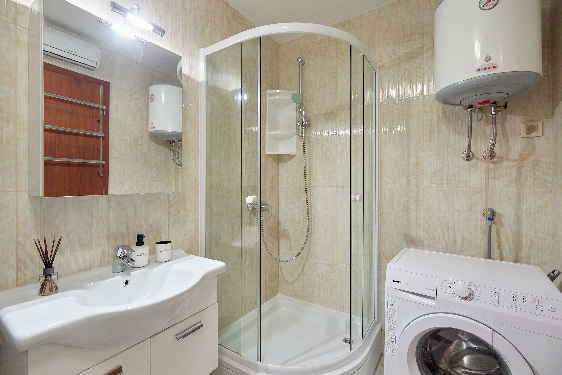 A bathroom with a glass-enclosed shower, a sink, a washing machine, and a toilet.