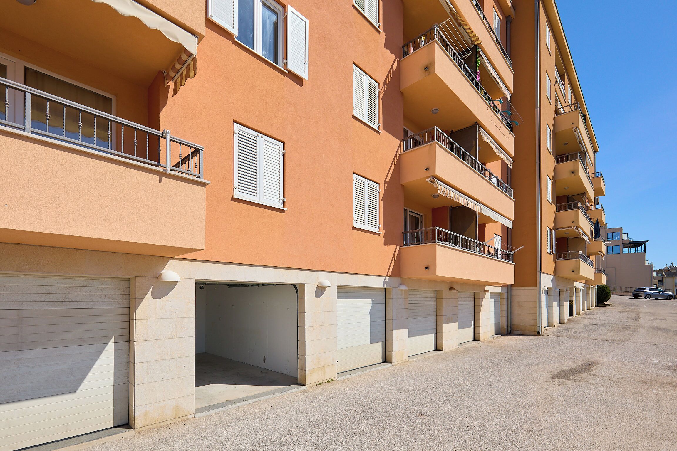 Um edifício residencial com vários andares, varandas, portões de garagem e um céu limpo.