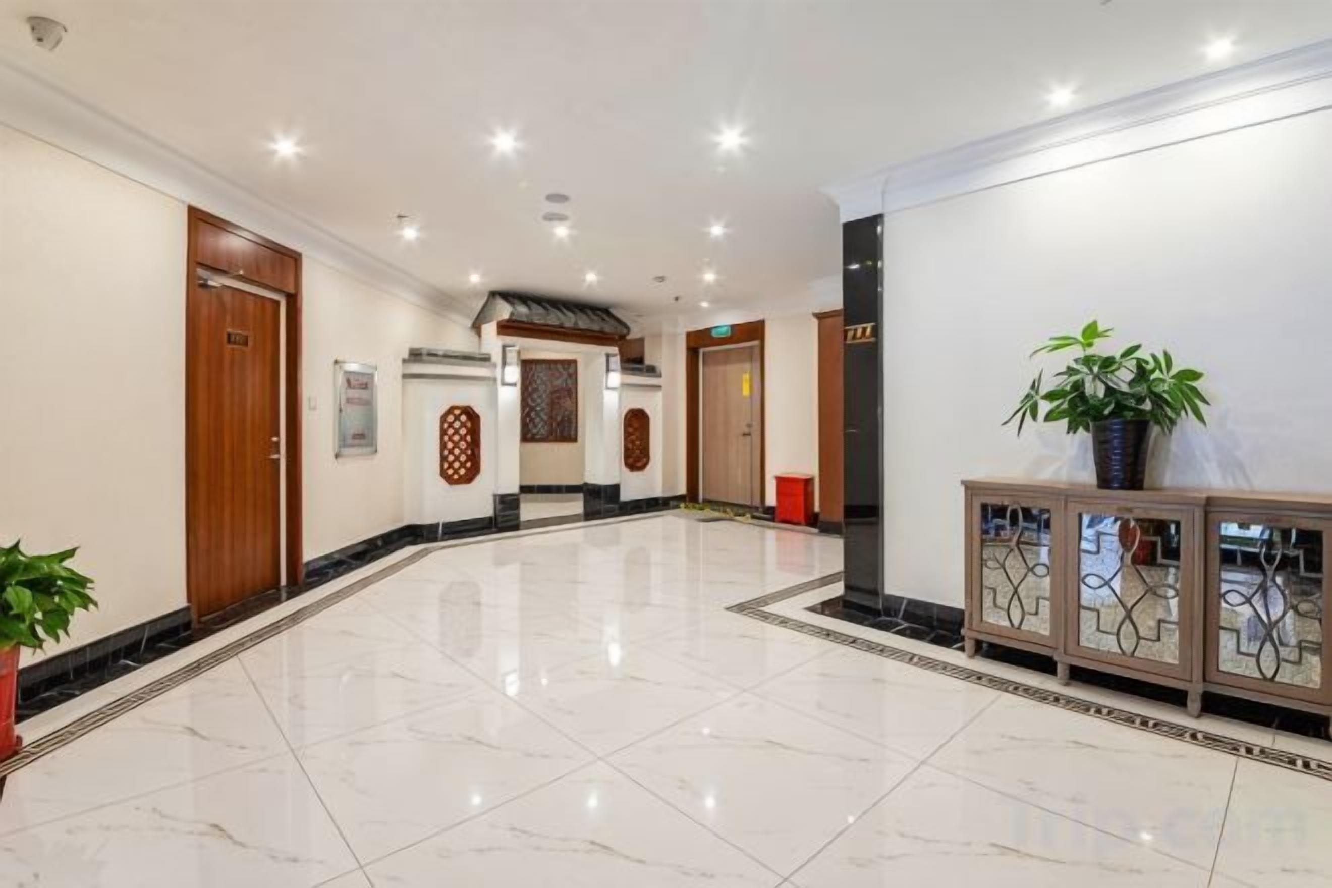 Um saguão de hotel com piso de mármore, portas de madeira, balcão de recepção e um vaso com planta.