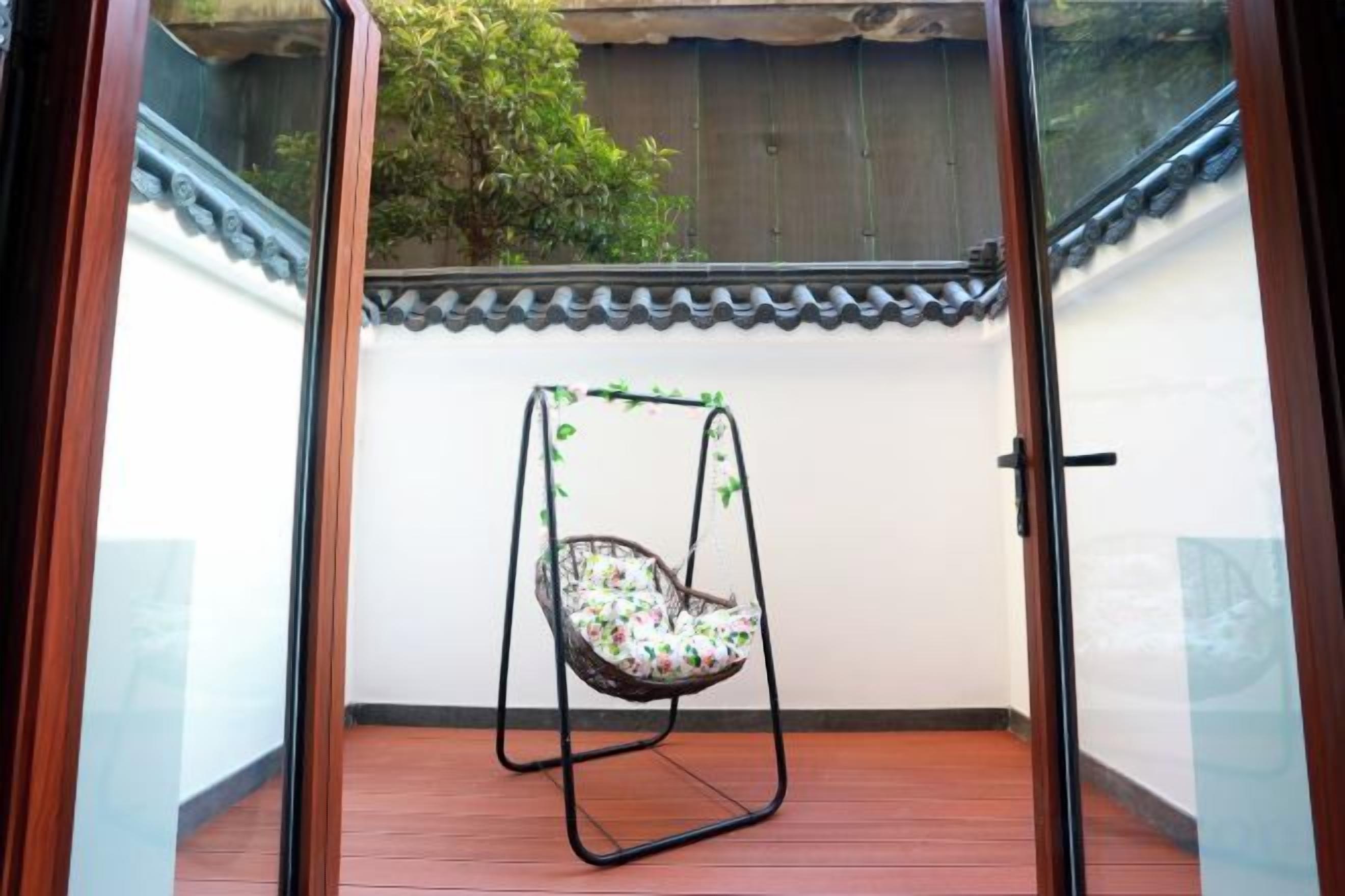 Una habitación con piso de madera, pared blanca con cornisa decorativa y una silla colgante con cojín floral.