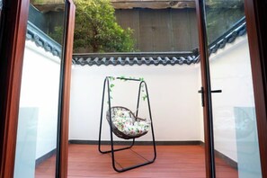 Una habitación con piso de madera, pared blanca con cornisa decorativa y una silla colgante con cojín floral.