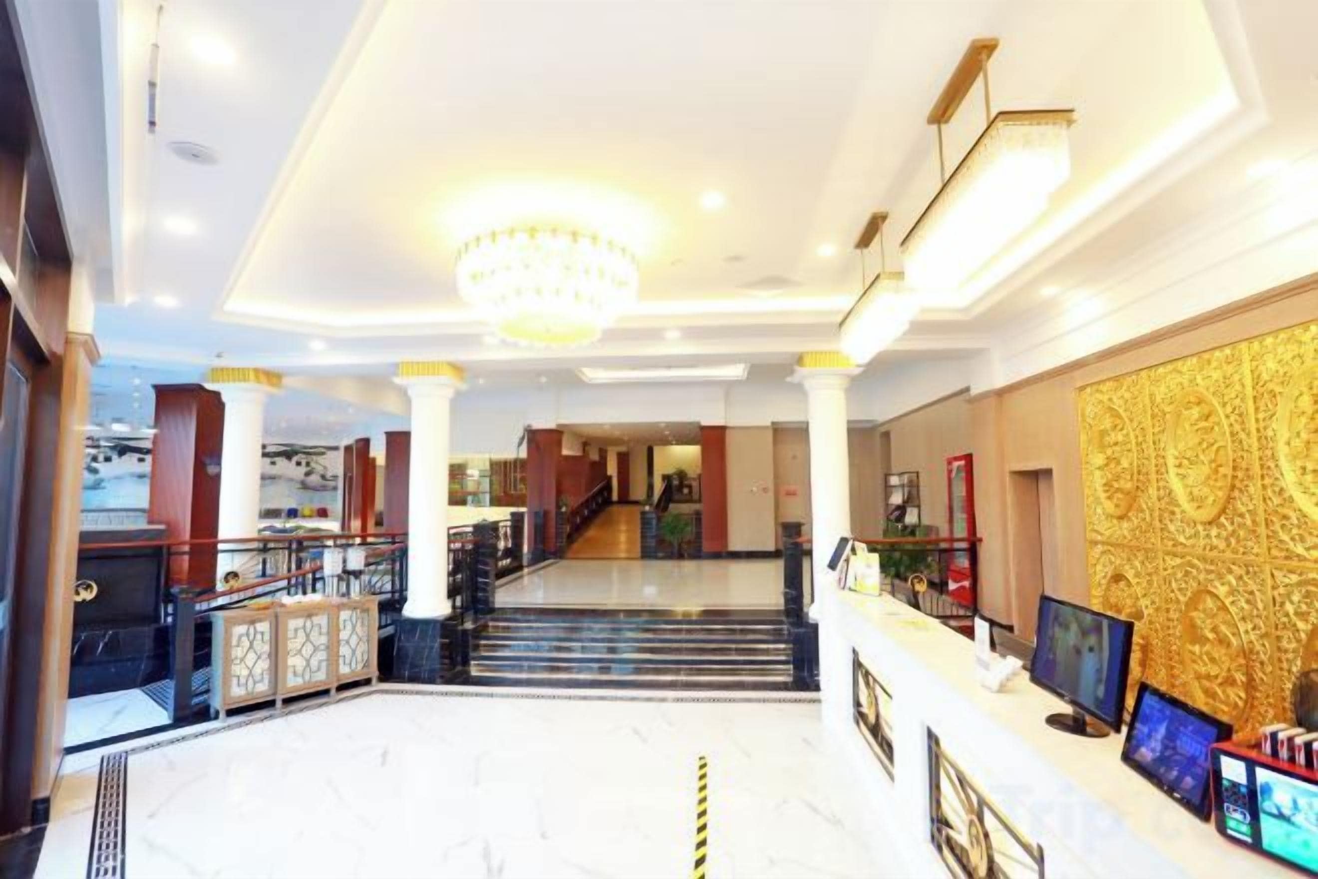 A hotel lobby with a grand staircase, a reception desk, and a chandelier.