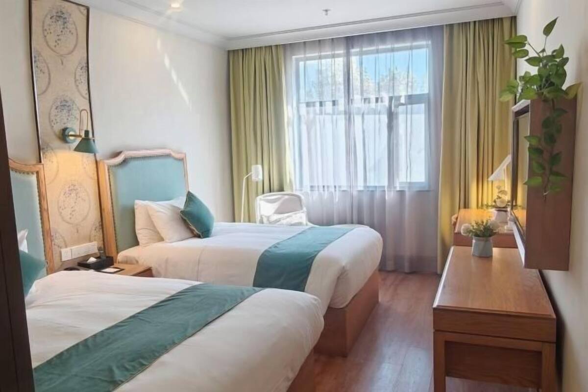 Ett hotellrum med två sängar, ett nattduksbord, en spegel och ett fönster med gardiner.