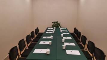 Un salón de conferencias con una mesa larga, sillas y una planta.