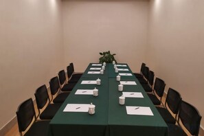 Un salón de conferencias con una mesa larga, sillas y una planta.