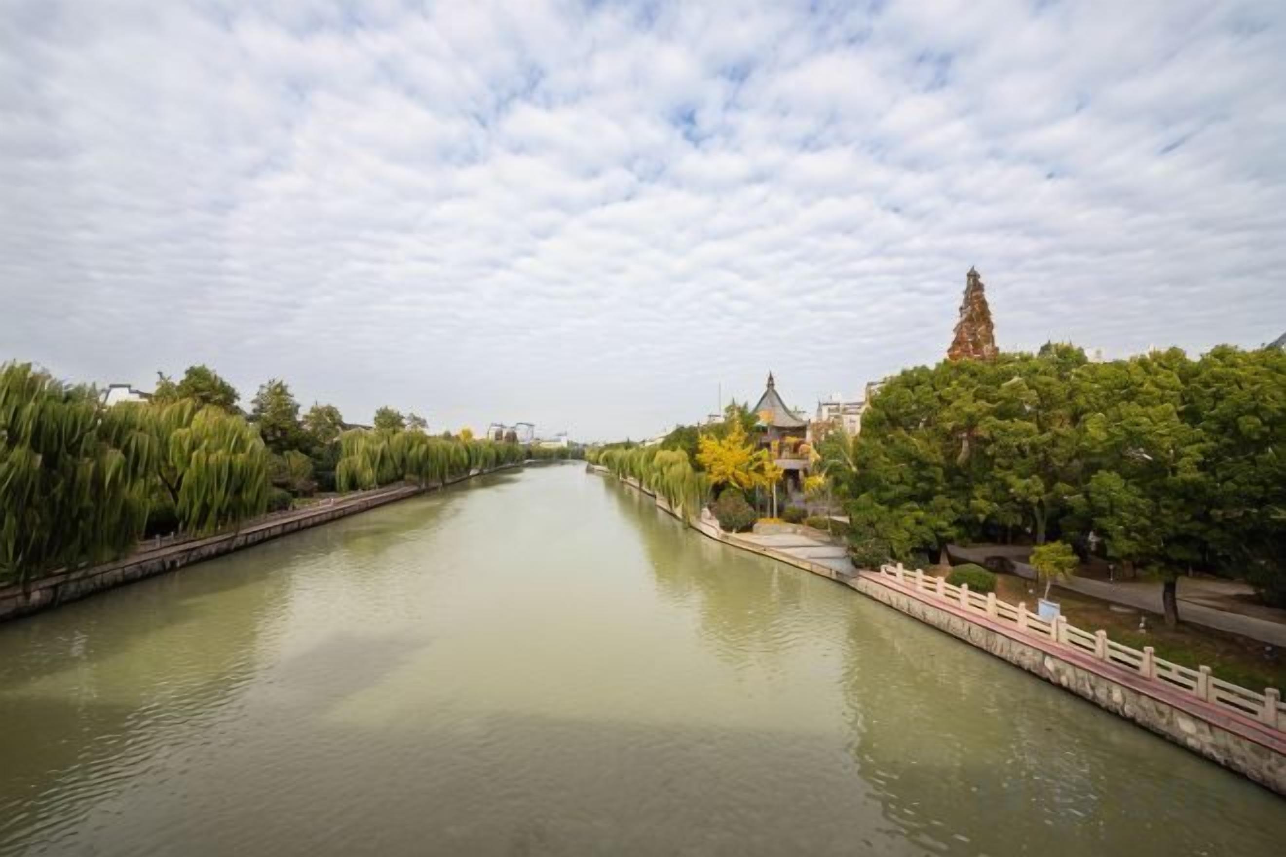 A river with a bridge and trees on one side, and a building with a tower on the other.