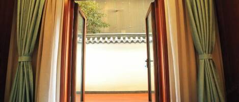 A room with a sliding glass door leading to a balcony, wooden flooring, and a tiled floor.
