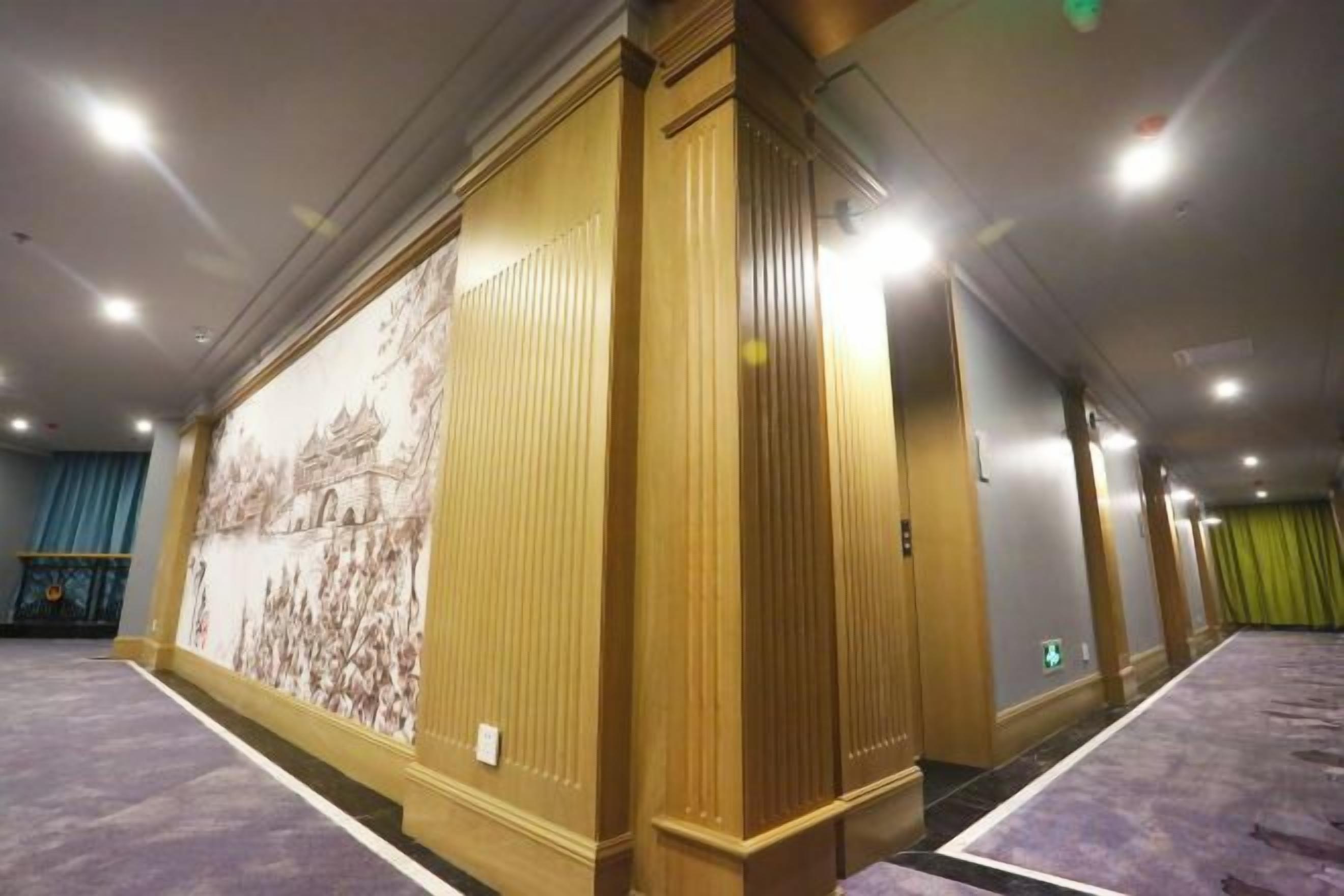 Un pasillo de hotel con un gran mural en la pared, piso alfombrado y una serie de puertas.