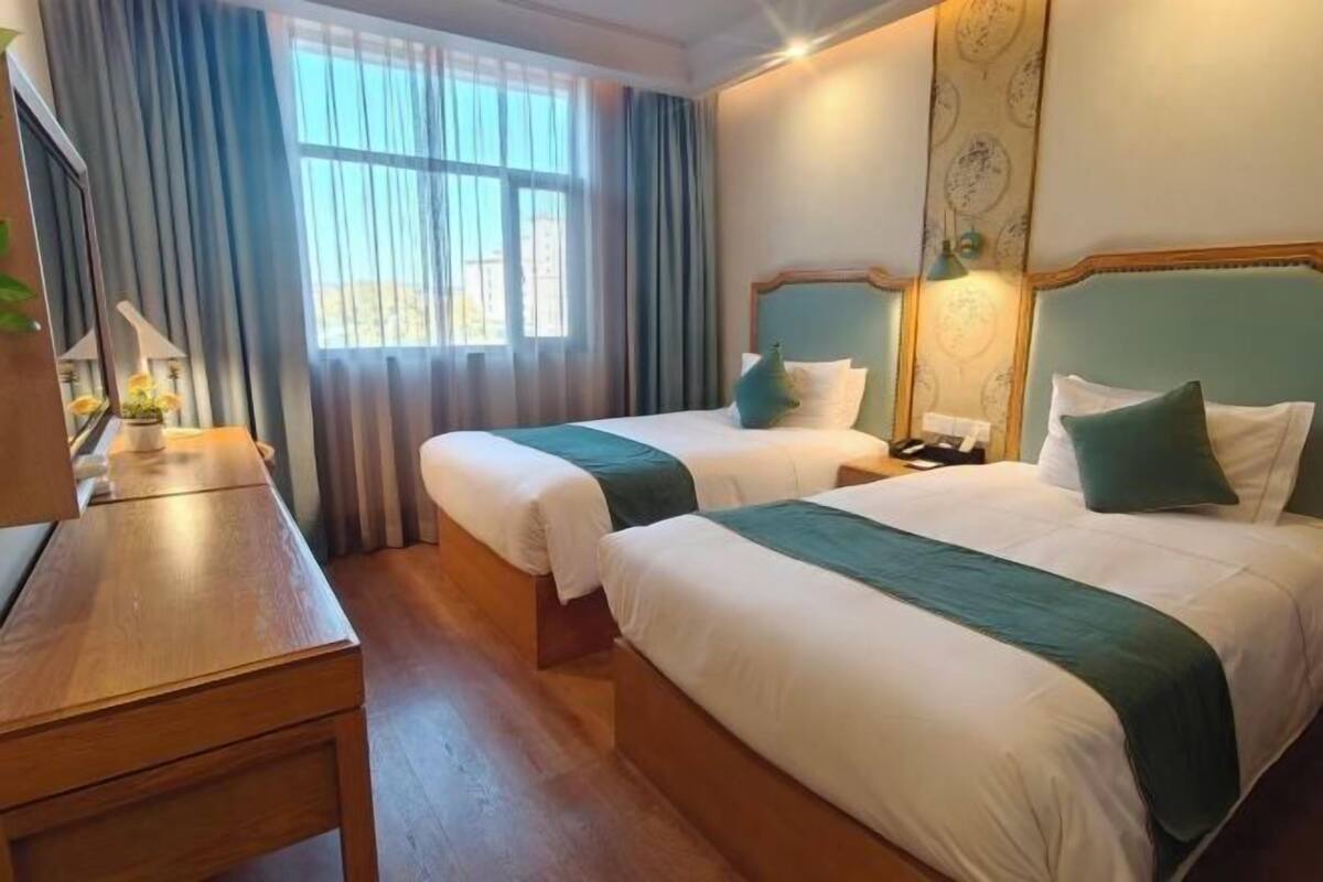 Ett hotellrum med två sängar, ett skrivbord i trä, ett nattduksbord och ett fönster med gardiner.
