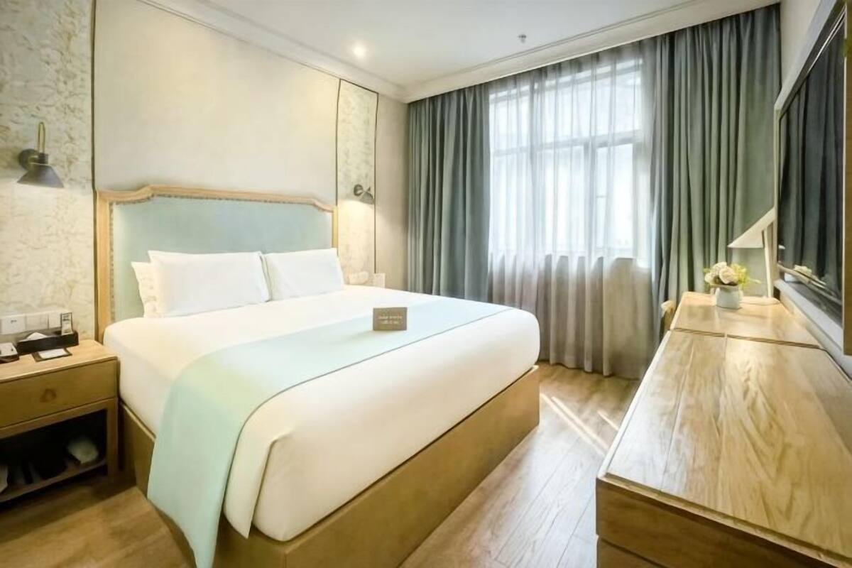Ett hotellrum med en stor säng, ett nattduksbord, en lampa och utsikt över omgivningarna.