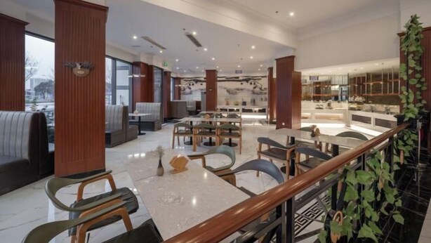 Un restaurante moderno con techos altos, pilares de madera y diversas opciones de asientos, incluyendo mesas y cabinas.