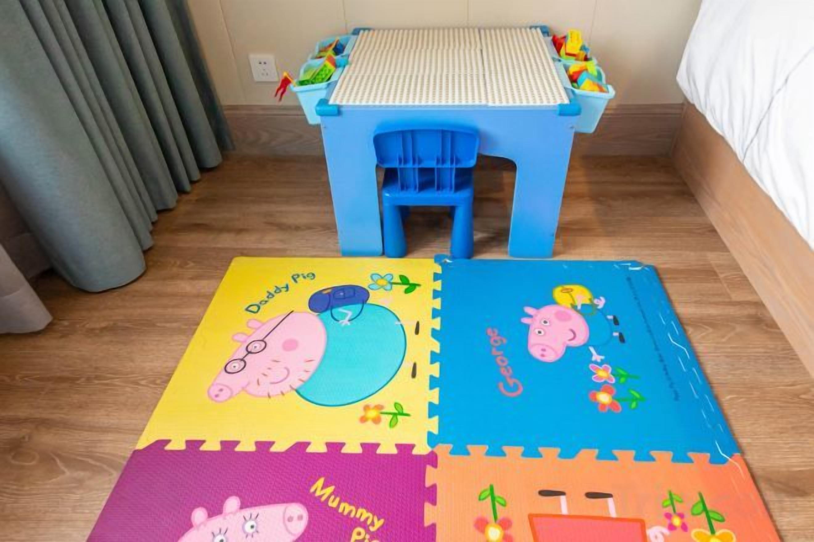 Quarto com mesa azul e tapete colorido com personagens de animais.