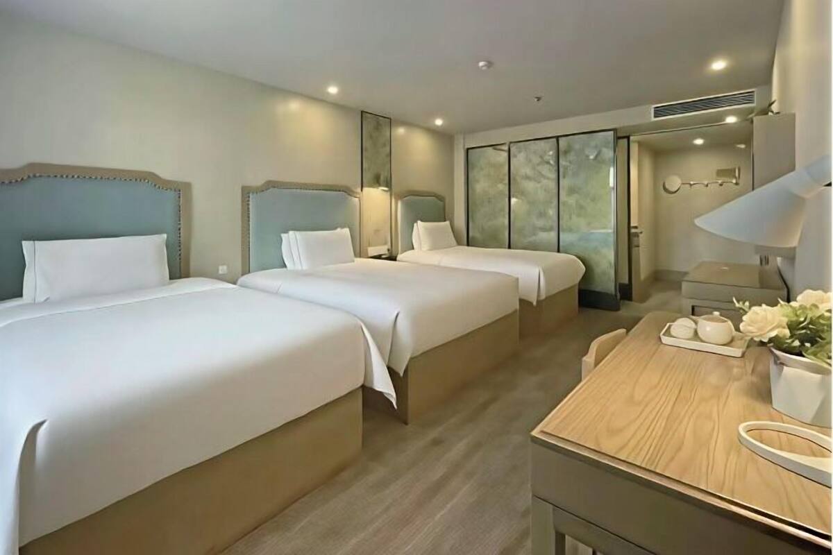 Ett hotellrum med två sängar, ett skrivbord i trä, en spegel och ett fönster med utsikt.