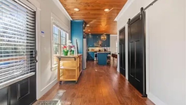 Un pasillo con piso de madera, una zona de cocina con armarios azules y una puerta negra.